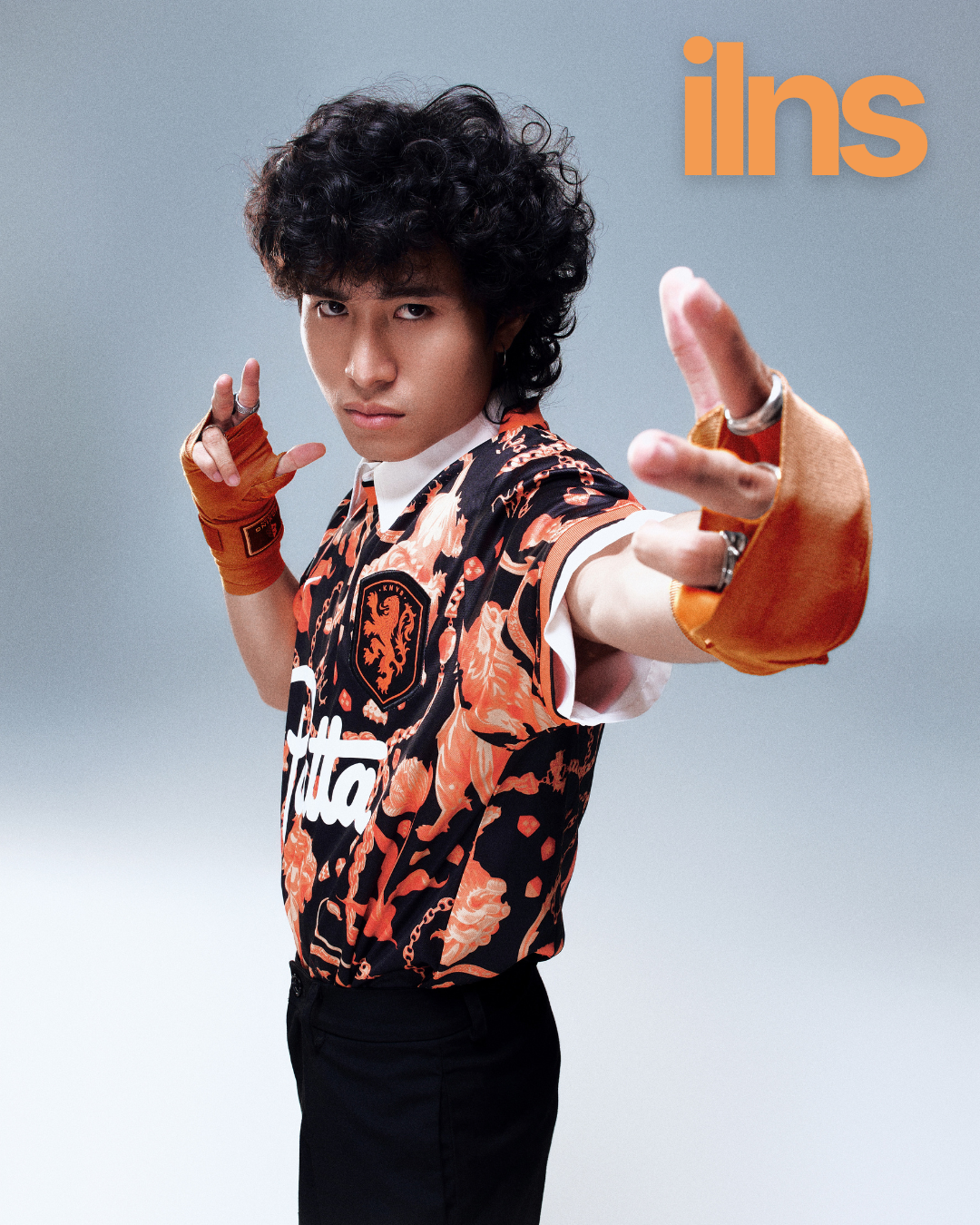 Person wearing an orange and black patterned shirt with 'Futura' branding, posing against a gray background.
