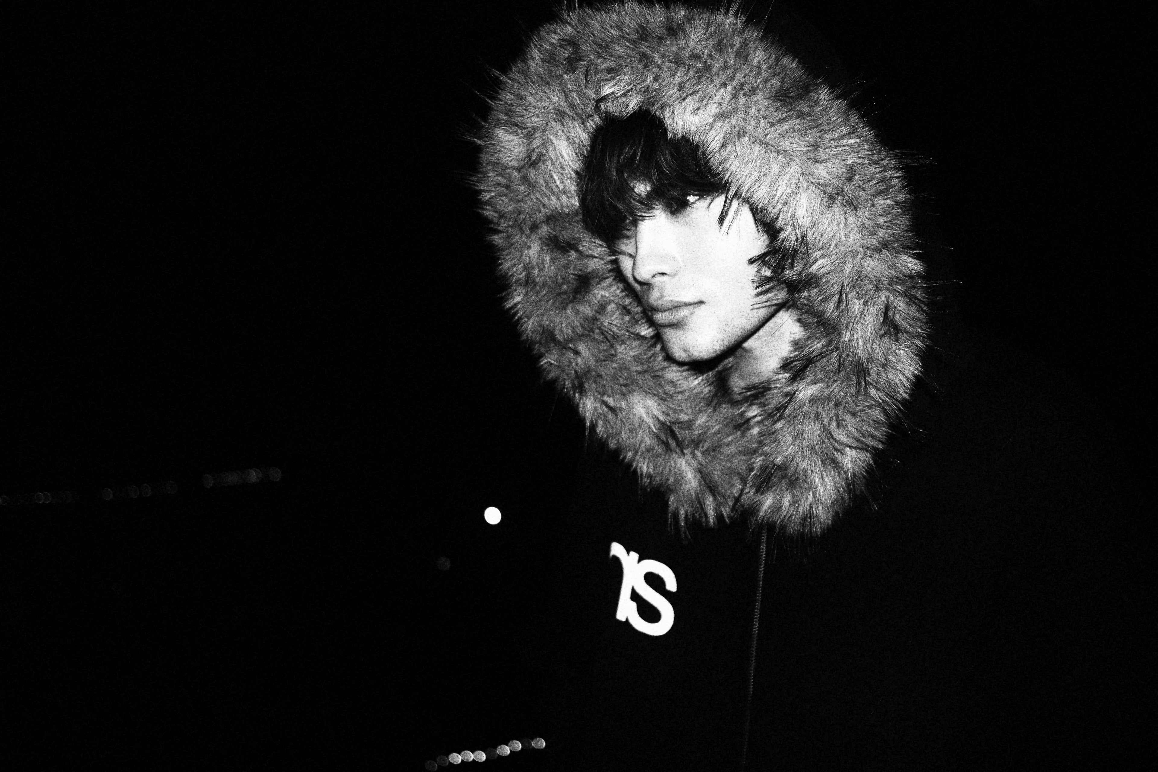 Person wearing a dark coat with a fur-lined hood against a black background